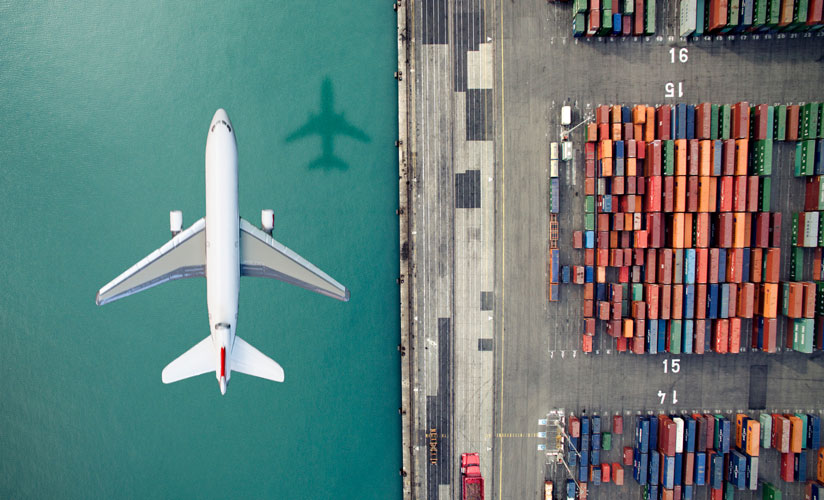 An aerial view of an airplane going over a port harbor filled with many large and colorful shipping containers